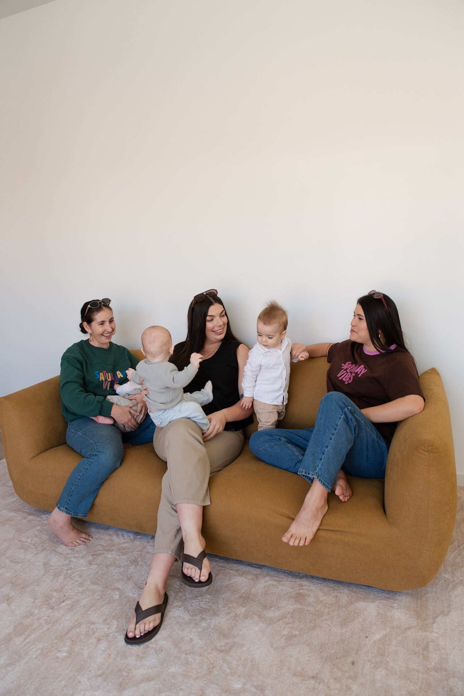 Breastfeeding Mums chatting on a couch with their babies and wearing Saturday Vibes. 