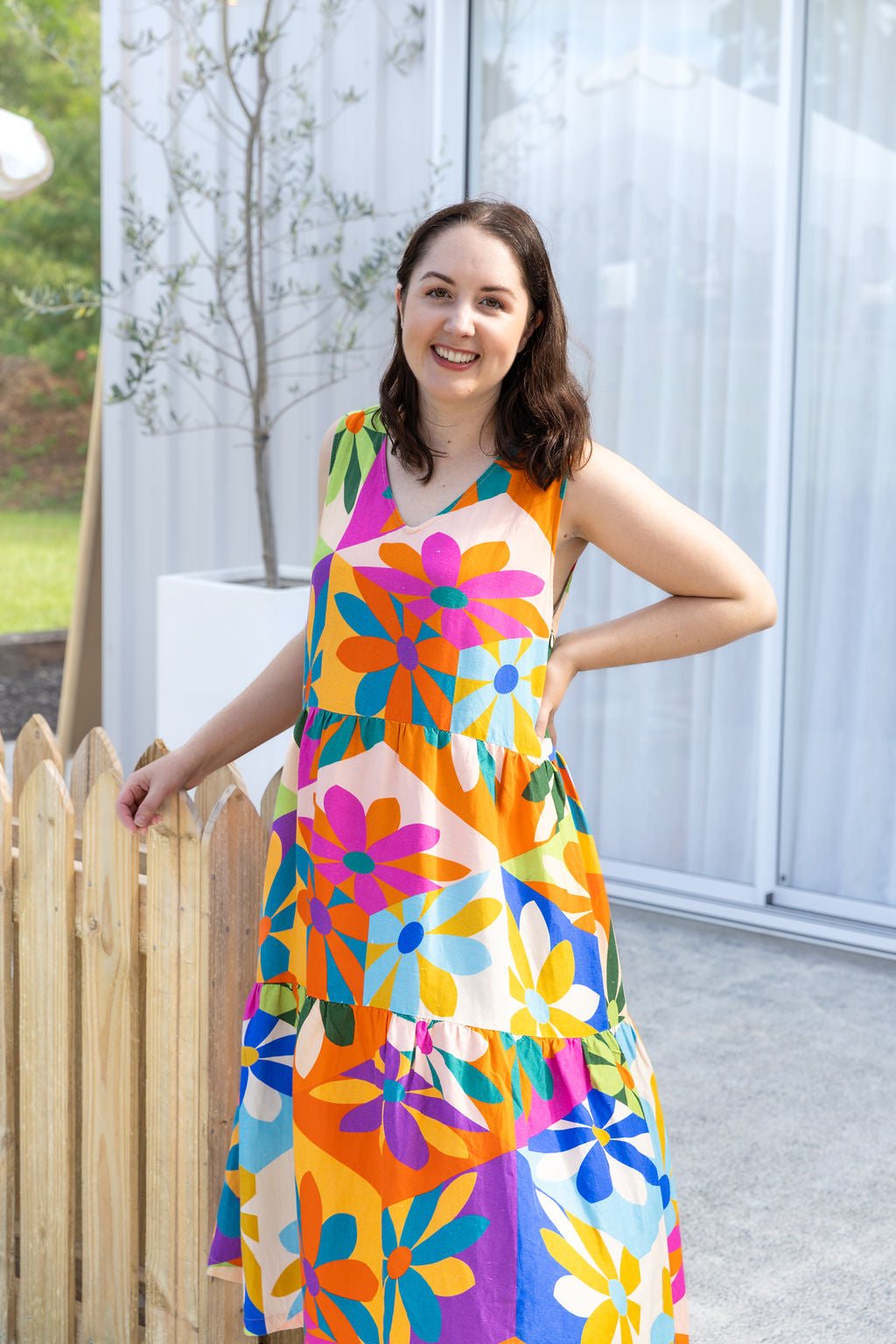 Woman wearing a colorful floral dress standing outdoors near a wooden fence.