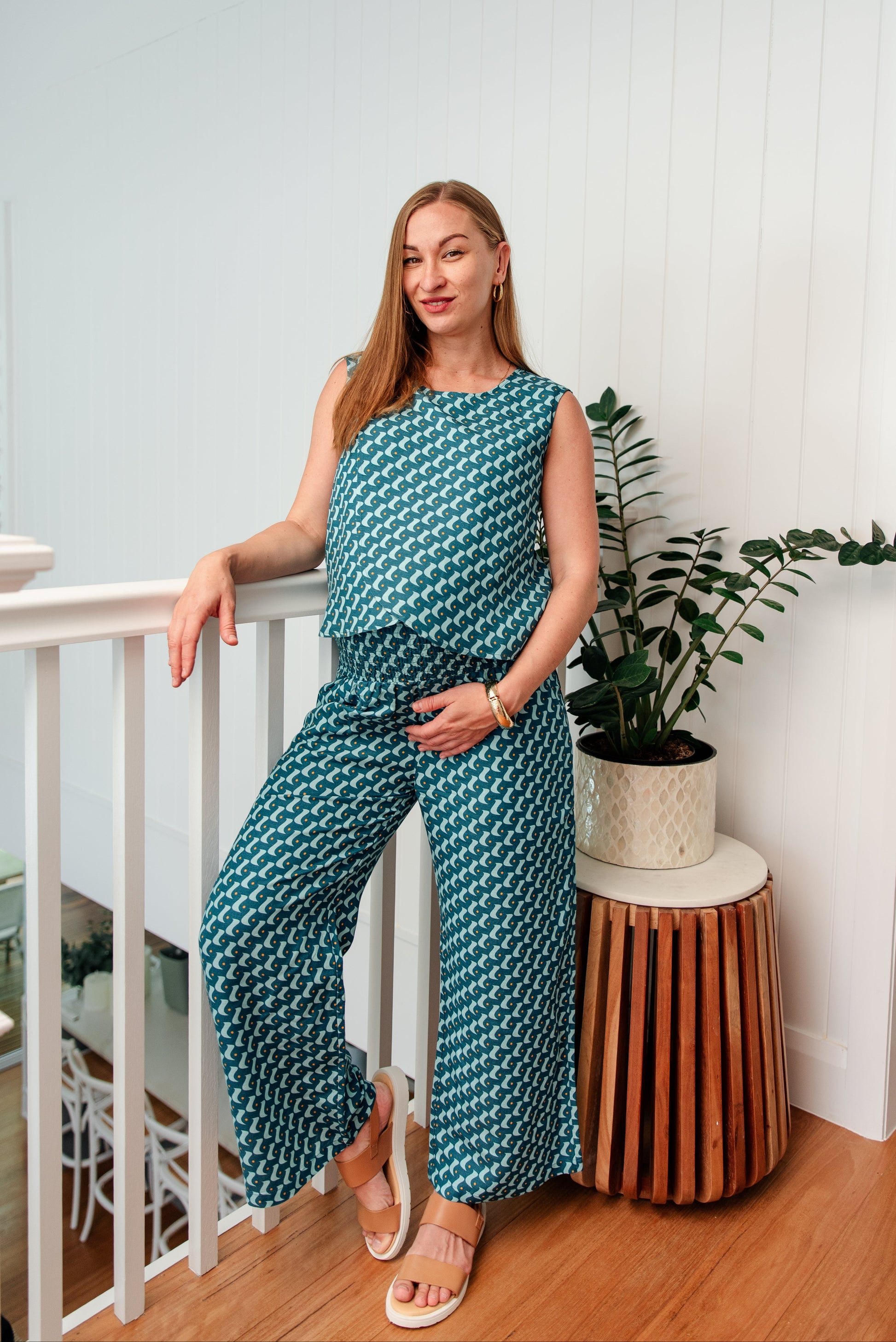 Woman in a teal patterned jumpsuit standing in a home interior.